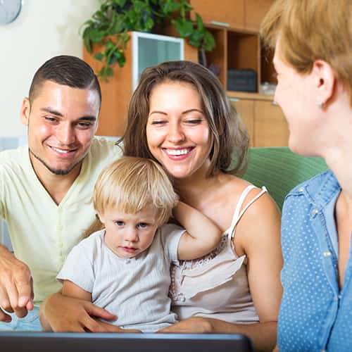 Young parents and toddler in home looking at laptop screen with home visitor.