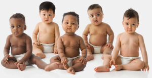 A group of five infants of differing races and ethnicities sit side-by-side on the floor in front of a white background.
