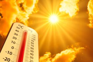 A blazing yellow sun shines down from a golden sky, surrounded by a handful of clouds and an outdoor thermometer registering a very high temperature.