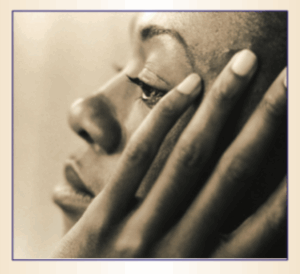 A black woman in profile holds her hand to her cheek and temple.