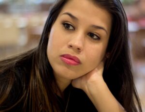 A young dark-haired woman sits alone reflecting on her day.