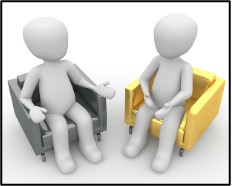 Two people sit in chairs facing each other, talking.