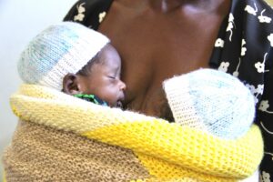 Two newborn babies in knit hats rest against an adult's chest, wrapped together in a yellow blanket. (Alternative text created using Microsoft Copilot)